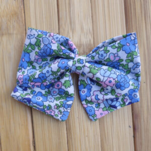 Lazo infantil con estampado floral en tonos azul, rosa y verde sobre fondo de madera.