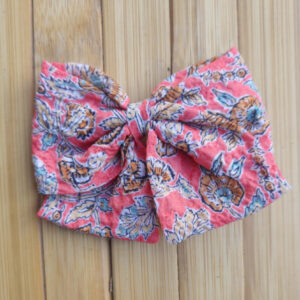 Lazo infantil con estampado floral vintage en tonos coral, azul y mostaza sobre fondo de madera