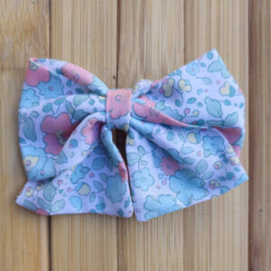 Lazo infantil con estampado floral en tonos pastel azul y rosa sobre fondo de madera.
