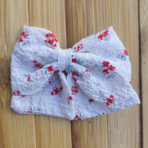Lazo blanco con estampado floral rojo sobre fondo de madera, accesorio de moda infantil Sutier.
