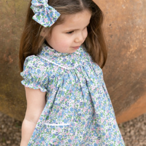 Niña con vestido floral azul y lazo a juego, colección de moda infantil Sutier.