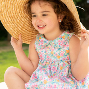 Moda infantil de verano: niña disfrutando junto a la piscina con vestido estampado de flores.