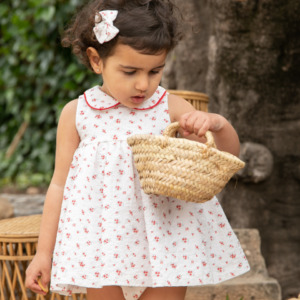 Niña con vestido blanco con flores rojas y cesto de mimbre, estilo delicado y natural de Sutier.