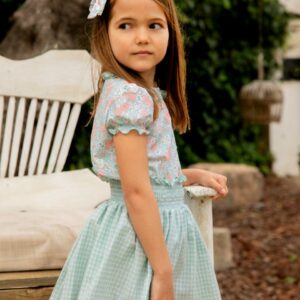 Niña de perfil con conjunto floral y falda verde de cuadros vichy, moda infantil de la colección Samba