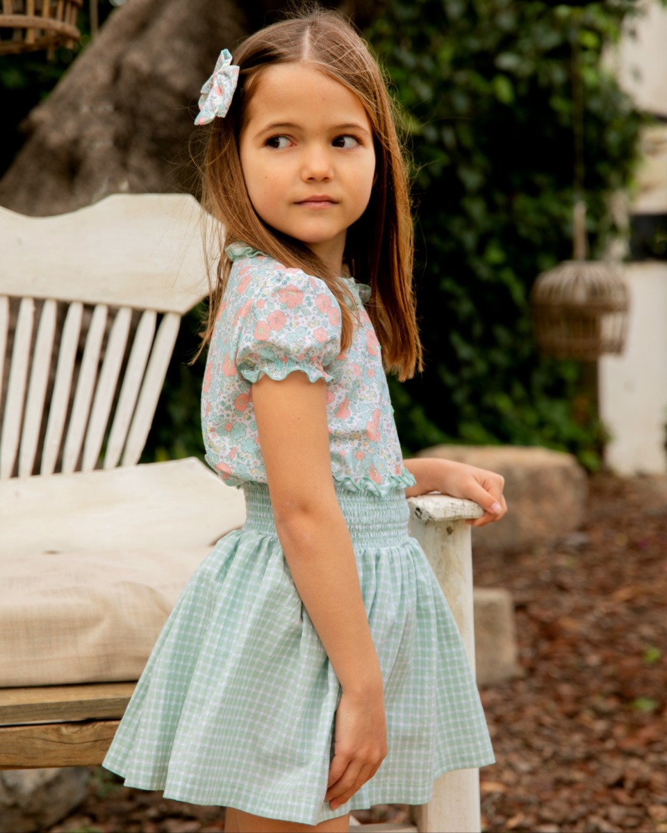 Niña de perfil con conjunto floral y falda verde de cuadros vichy, moda infantil de la colección Samba