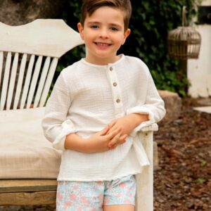 Niño posando con una camiseta blanca y pantalones cortos florales de la colección Samba, sentado en un banco al aire libre.