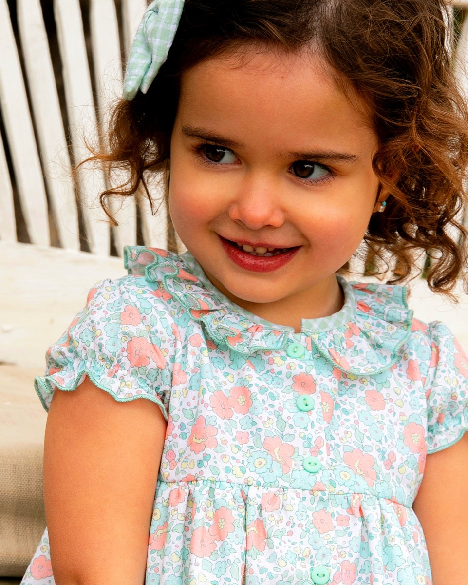 Niña usando un vestido de flores de la colección Samba, mostrando detalles de botones y un elegante lazo en el cabello.