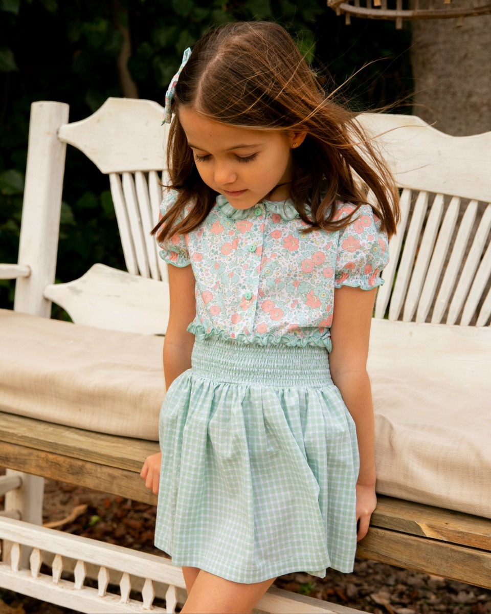 Niña con conjunto infantil de blusa floral y falda de cuadros verdes, de la colección Samba