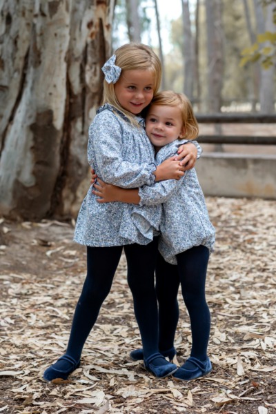 Dos niñas abrazadas con conjuntos florales azules de manga larga, moda infantil de Sutier