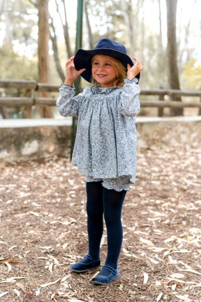 Niña sonriente con conjunto floral azul y sombrero a juego, moda infantil elegante de Sutier