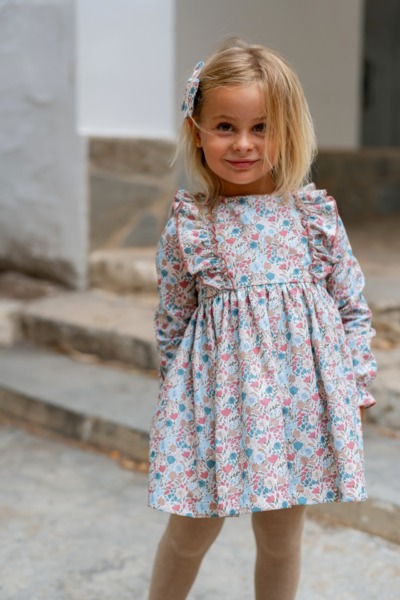 Niña rubia con vestido de niña de manga larga, volantes y estampado floral rosa y azul de Sutier