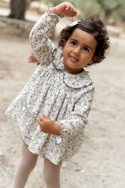 Niña con vestido floral blanco de manga larga jugando al aire libre, moda infantil Sutier