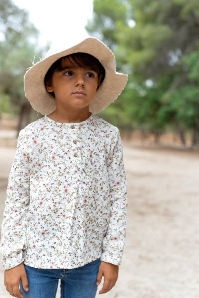Niño con blusa floral blanca y sombrero beige, moda infantil Sutier