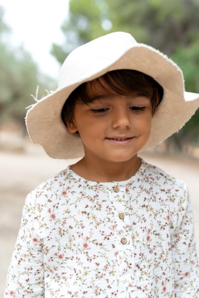 Niño con blusa floral blanca de manga larga y sombrero beige, moda infantil Sutier