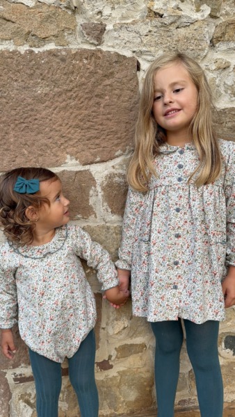 Dos niñas con conjuntos florales de Sutier posando de la mano junto a una pared de piedra, moda infantil española
