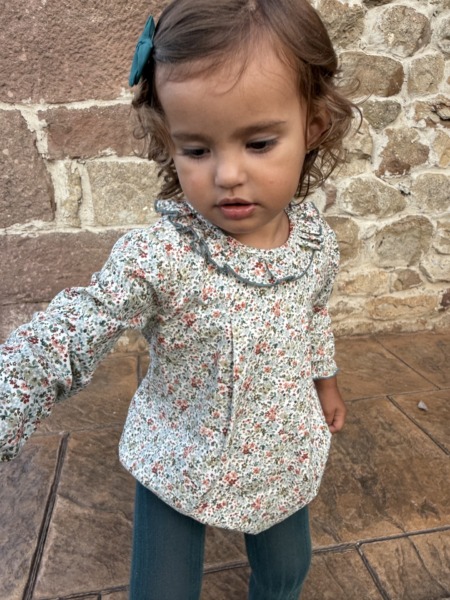 Niña con blusa floral de manga larga y lazo en el pelo verde, moda infantil Sutier